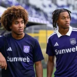 Twee jonge voetballers in paarse Anderlecht-tenues staan naast een voetbalveld.