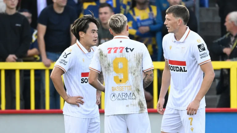 Drie spelers van Westerlo in witte wedstrijdshirts die elkaar op het veld opzoeken.