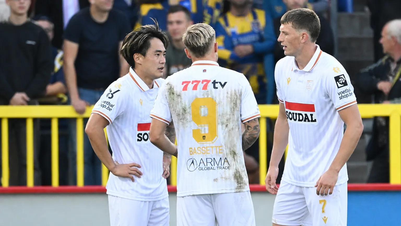 Drie spelers van Westerlo in witte wedstrijdshirts die elkaar op het veld opzoeken.