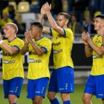 Een groep STVV-spelers in gele shirts en blauwe broekjes applaudisseert naar de tribune.