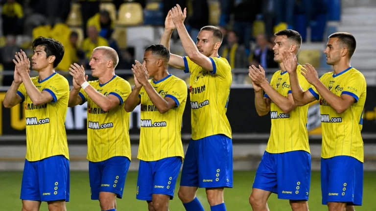 Een groep STVV-spelers in gele shirts en blauwe broekjes applaudisseert naar de tribune.