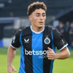 Een Club Brugge-speler warmt op in een zwart-blauw shirt op het veld.