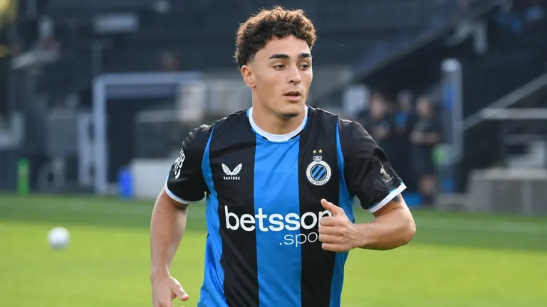 Een Club Brugge-speler warmt op in een zwart-blauw shirt op het veld.