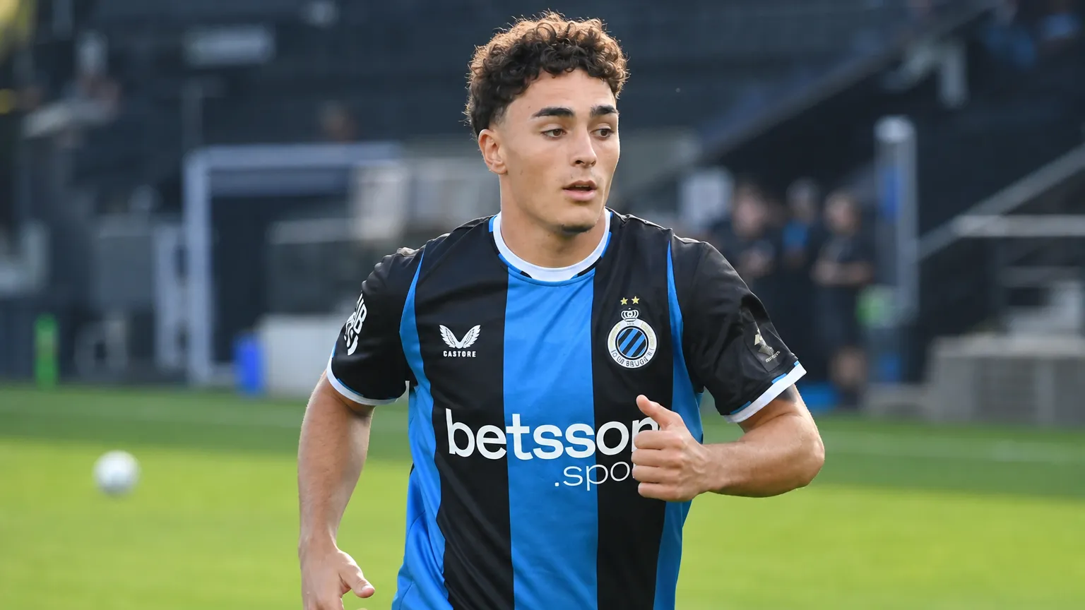 Een Club Brugge-speler warmt op in een zwart-blauw shirt op het veld.