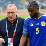 Een Curaçao-speler en een niet-spelend staflid langs de zijlijn van een voetbalstadion.