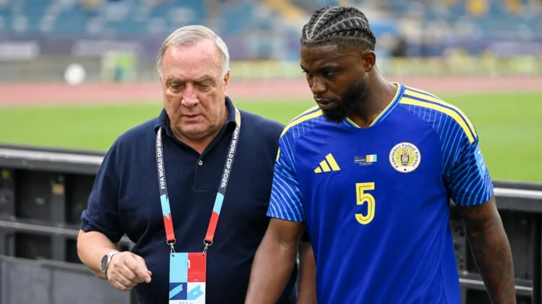 Een Curaçao-speler en een niet-spelend staflid langs de zijlijn van een voetbalstadion.