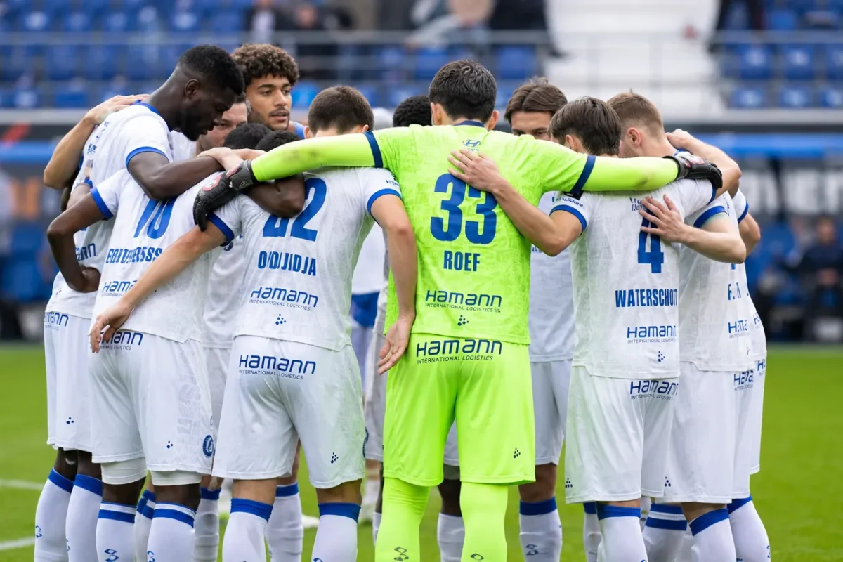 Een groep KAA Gent-spelers vormt een hechte kring op het veld voor de wedstrijd.
