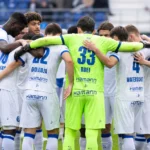 Een groep KAA Gent-spelers vormt een hechte kring op het veld voor de wedstrijd.