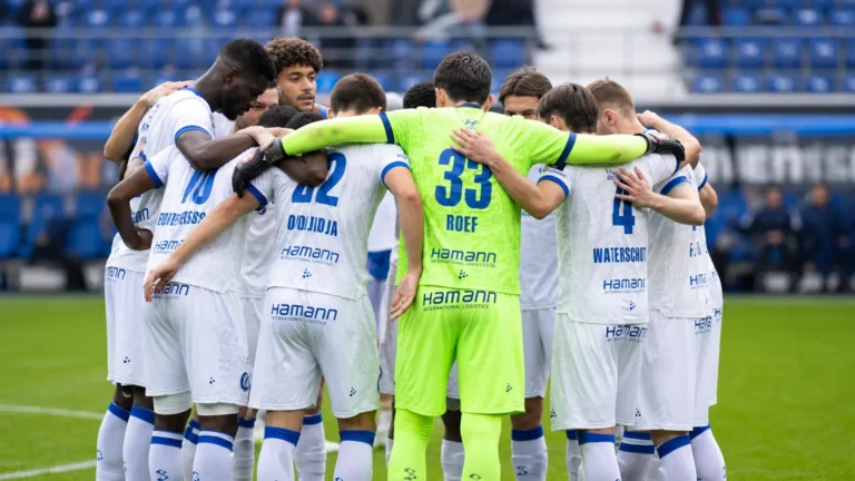 Een groep KAA Gent-spelers vormt een hechte kring op het veld voor de wedstrijd.