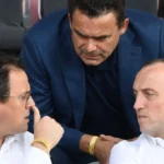 Drie niet-spelende clubvertegenwoordigers in gesprek op de tribune van een stadion.