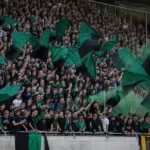 Een groep Cercle Brugge-supporters met groen-zwarte vlaggen en sjaals in de tribune.