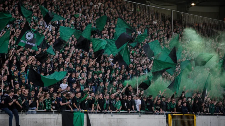 Een groep Cercle Brugge-supporters met groen-zwarte vlaggen en sjaals in de tribune.
