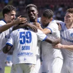 Een groep voetballers in witte tenues die elkaar op het veld omarmen.