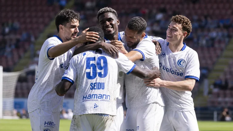 Een groep voetballers in witte tenues die elkaar op het veld omarmen.