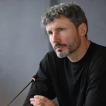 Mark van Bommel luistert aandachtig in een neutrale mediaruimte.