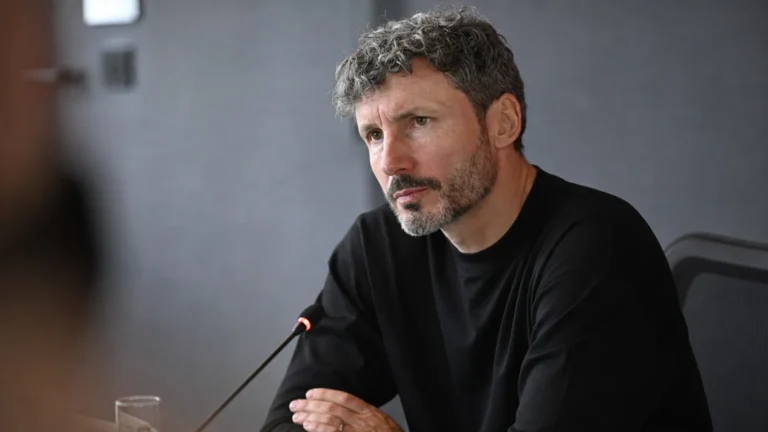 Mark van Bommel luistert aandachtig in een neutrale mediaruimte.