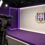 Een clubmedia-camera in een presentatiezone van RSC Anderlecht met één embleem aan de wand.