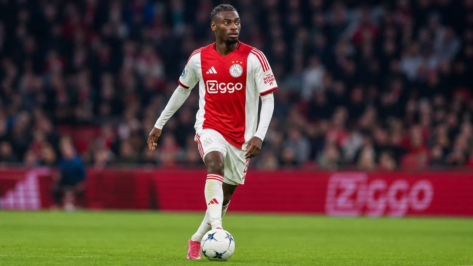 Jorthy Mokio controleert de bal op het middenveld in een Ajax-tenue.