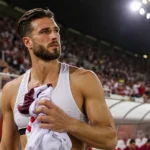 Wesley Hoedt staat met sportkleding in zijn hand langs een vol voetbalstadion.