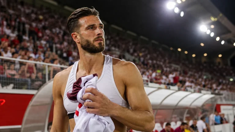 Wesley Hoedt staat met sportkleding in zijn hand langs een vol voetbalstadion.