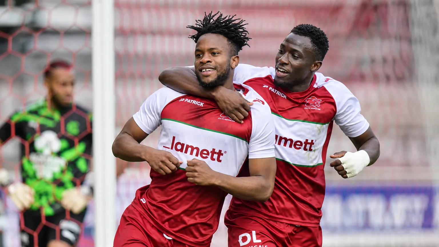Twee spelers van Zulte Waregem vieren een doelpunt nabij het doel.