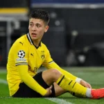 Kos Karetsas zit in zijn geel-zwarte Dortmund-tenue op het gras naast de zijlijn.