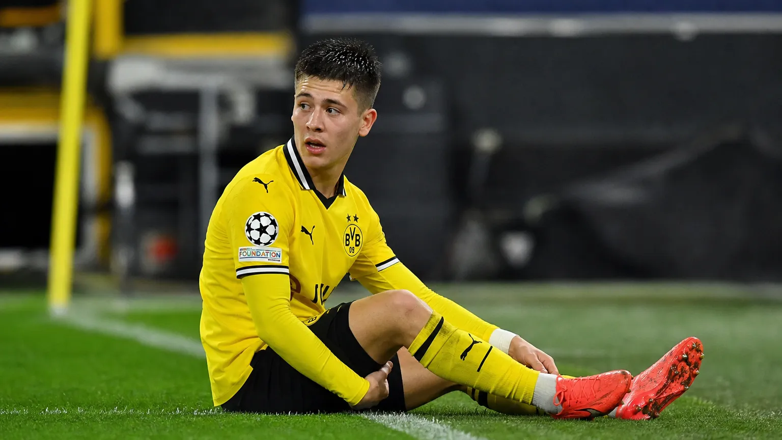 Kos Karetsas zit in zijn geel-zwarte Dortmund-tenue op het gras naast de zijlijn.