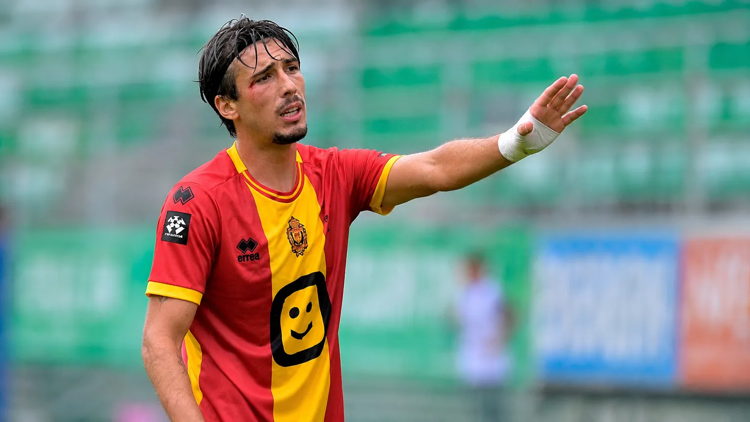 Een voetballer in een rood-geel shirt gebaart langs de rand van het veld.