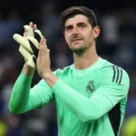 Thibaut Courtois applaudisseert in het doelmanstenue van Real Madrid aan de rand van het veld.