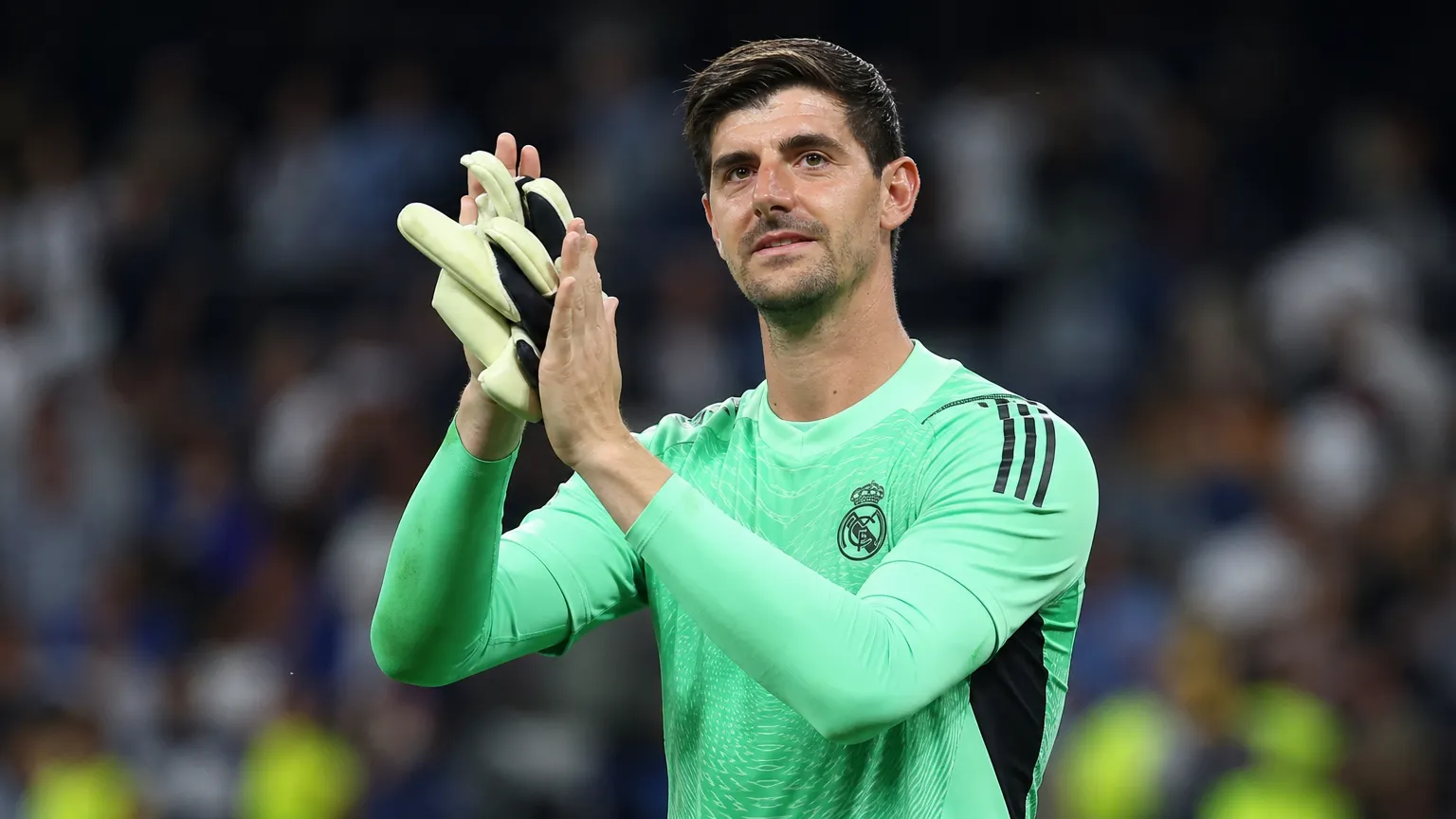 Thibaut Courtois applaudisseert in het doelmanstenue van Real Madrid aan de rand van het veld.