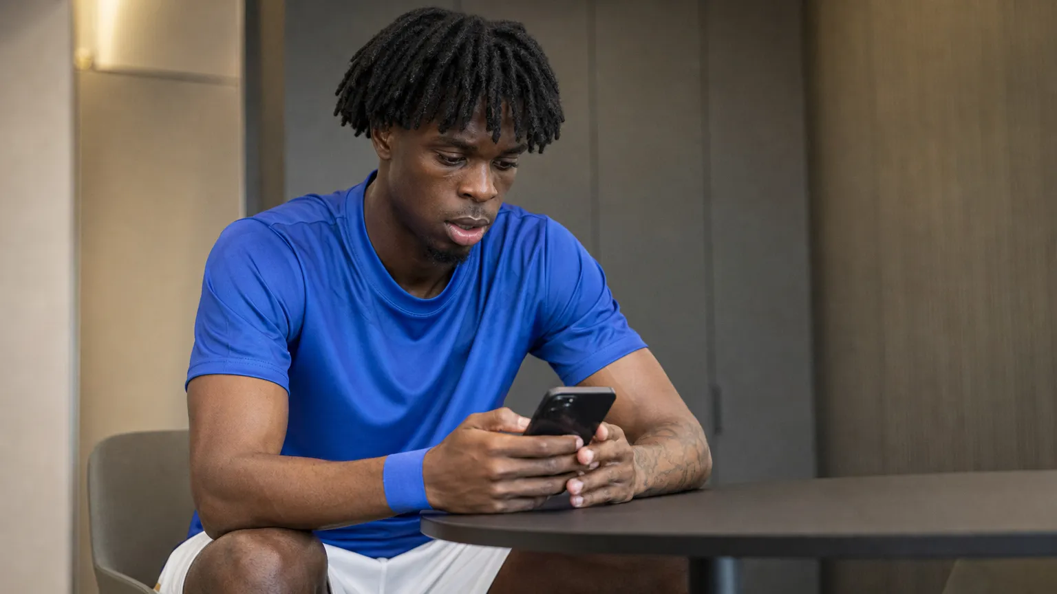 Ovie Ejaria bekijkt een smartphone in een neutrale binnenruimte.