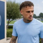 Noa Lang in neutrale sportkleding naast het trainingsveld van SSC Napoli, met een clubembleem op een vast bord.
