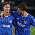 Twee Brighton-spelers in blauw-wit gestreepte wedstrijdshirts vieren samen een moment op het veld.