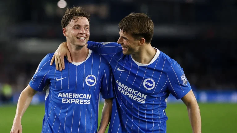 Twee Brighton-spelers in blauw-wit gestreepte wedstrijdshirts vieren samen een moment op het veld.