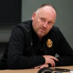 Fred Vanderbiest spreekt tijdens een persmoment aan een tafel in clubkleding.
