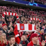 Een collectieve groep Bayern München-supporters applaudisseert met rood-witte sjaals op de tribune.