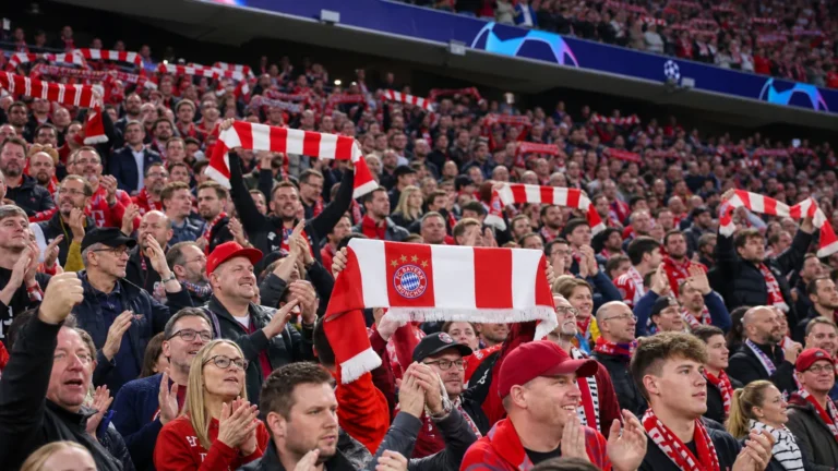Een collectieve groep Bayern München-supporters applaudisseert met rood-witte sjaals op de tribune.