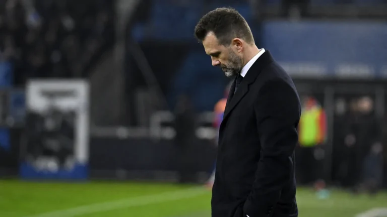 Een coach van Club Brugge in donkere jas langs de zijlijn na een Europese wedstrijd.
