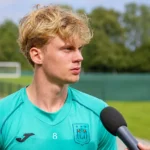 Cedric Hatenboer in een turquoise trainingstop tijdens een interview in openlucht.