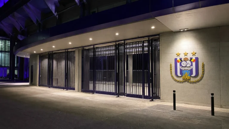 Verlichte ingang van Lotto Park met één Anderlecht-embleem aan de gevel.