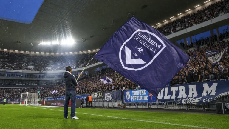 Supporters zwaaien met een grote donkerblauwe clubvlag in een vol stadion.