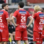 Een groep KV Kortrijk-spelers in rode wedstrijdkleding tijdens een nieuw moment naast het veld.