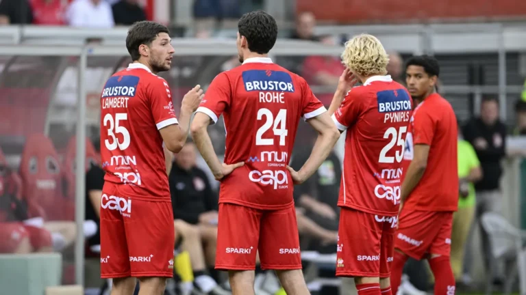 Een groep KV Kortrijk-spelers in rode wedstrijdkleding tijdens een nieuw moment naast het veld.