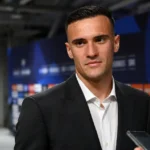 Aleksandar Stankovic in een donker pak in een neutrale mixed zone van een voetbalstadion.