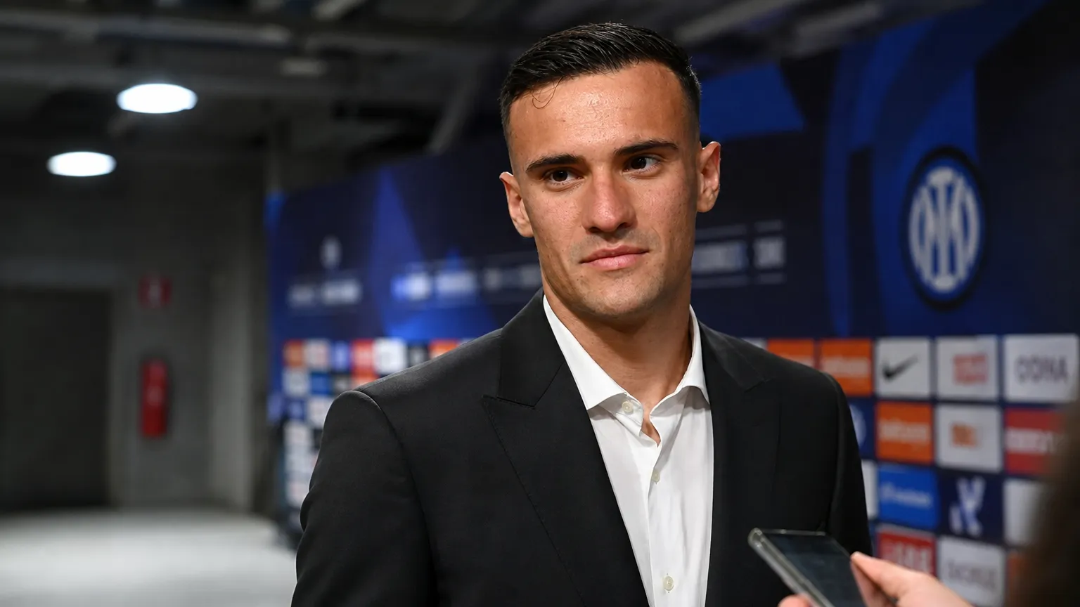 Aleksandar Stankovic in een donker pak in een neutrale mixed zone van een voetbalstadion.