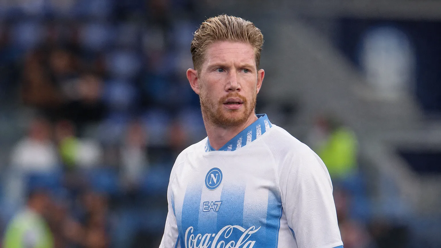 Een voetballer in een wit-blauw Napoli-tenue langs de zijlijn van een stadion.