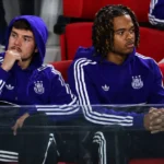 Een groep Anderlecht-spelers in paarse trainingskleding kijkt vanuit de stadionzitjes toe.