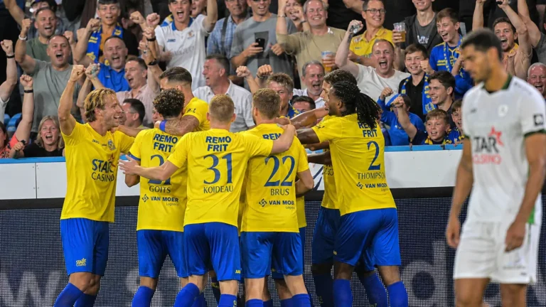 Een groep voetballers in gele shirts viert samen voor een volle thuistribune.