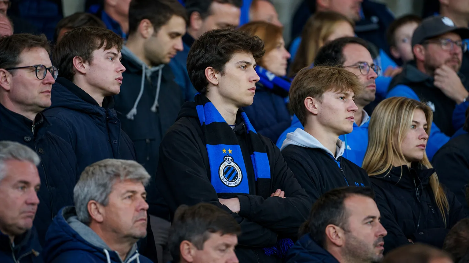 Een groep Club Brugge-supporters met blauw-zwarte sjaals op de tribune.