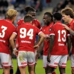 Een groep spelers van Standard Luik in rode shirts overlegt op het veld.